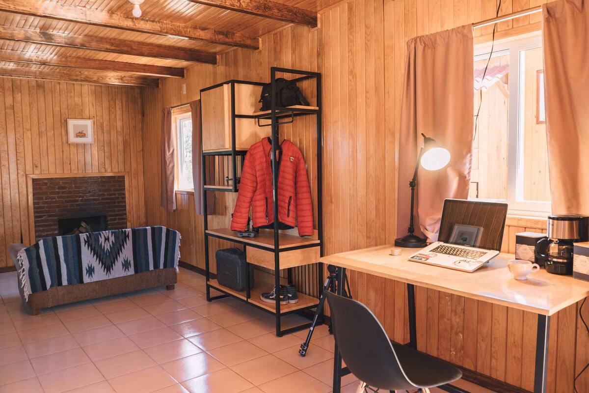 Une pièce chaleureuse avec un décor en bois, une cheminée, un lit superposé, un bureau avec un ordinateur portable et une machine à café.