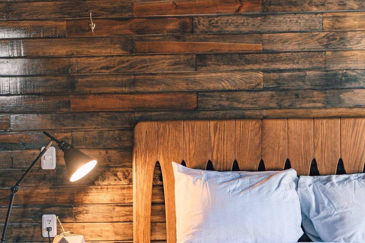 Une tête de lit en bois au design original, une lampe de chevet et une prise électrique sur une table de chevet en bois.