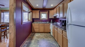 A kitchen with wooden cabinets, a white refrigerator, and a window with blinds. - Riverview Townhouse I in Downtown Alexandria Bay (Alexandria Bay)