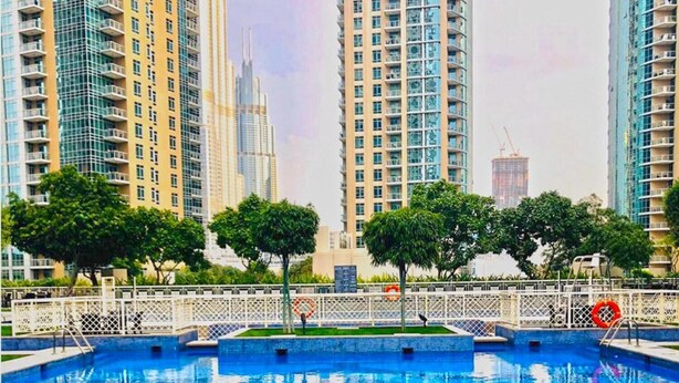 A swimming pool with a white fence and trees in the background. - Spectacular 2BR With Burj Khalifa Fountain View (Dubai)