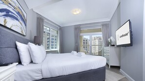 A modern hotel room with a large bed, a flat-screen TV, and a city view. - 2BR on Palm Jumeirah With Beach and Complimentary Golf (Dubai)