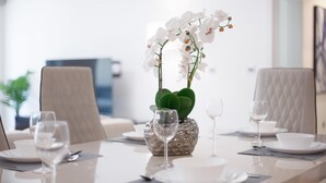 A dining table set with white plates, silverware, and wine glasses, with a decorative orchid centerpiece. - 2BR on Palm Jumeirah With Beach and Complimentary Golf (Dubai)