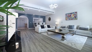 A modern living room with a white sofa set, a coffee table, and a dining area with a kitchen in the background. - 2BR on Palm Jumeirah With Beach and Complimentary Golf (Dubai)
