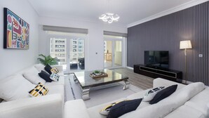 A modern living room with a sofa set, a glass coffee table, a flat-screen TV, and a decorative light fixture. - 2BR on Palm Jumeirah With Beach and Complimentary Golf (Dubai)
