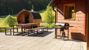 Een houten blokhut met een barbecue en een vat op het terras.