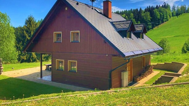 Een tweelaags houten huis met een schuin dak, een schotelantenne en een schoorsteen.