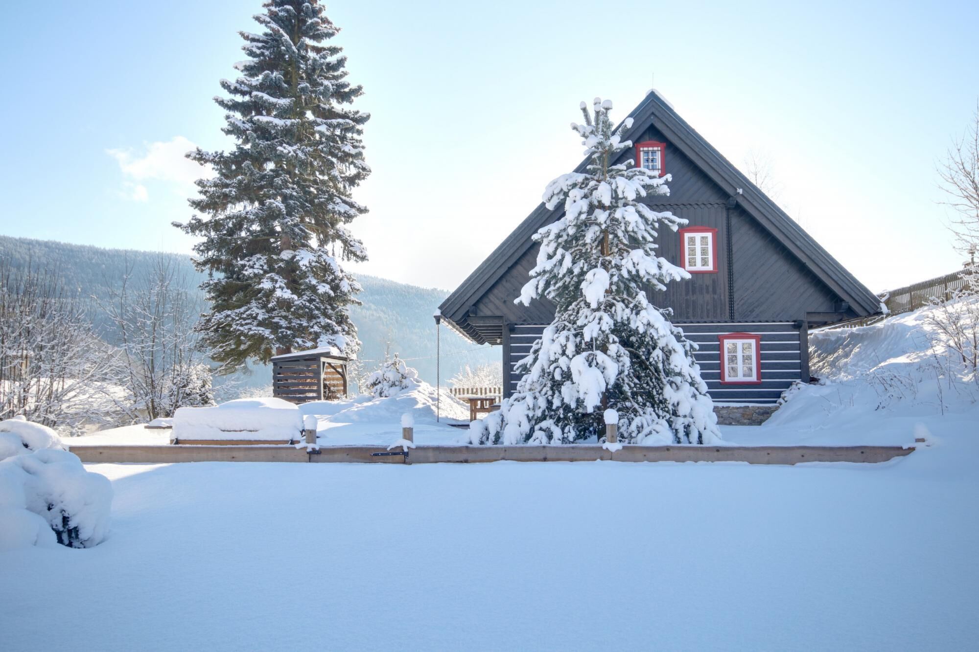 A wooden cabin with a sloped roof, surrounded by snow-covered trees and a clear sky.