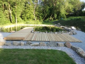 A wooden deck leading to a pond surrounded by rocks and grass. - Lesany Sljk425 in Le any (Lešany)