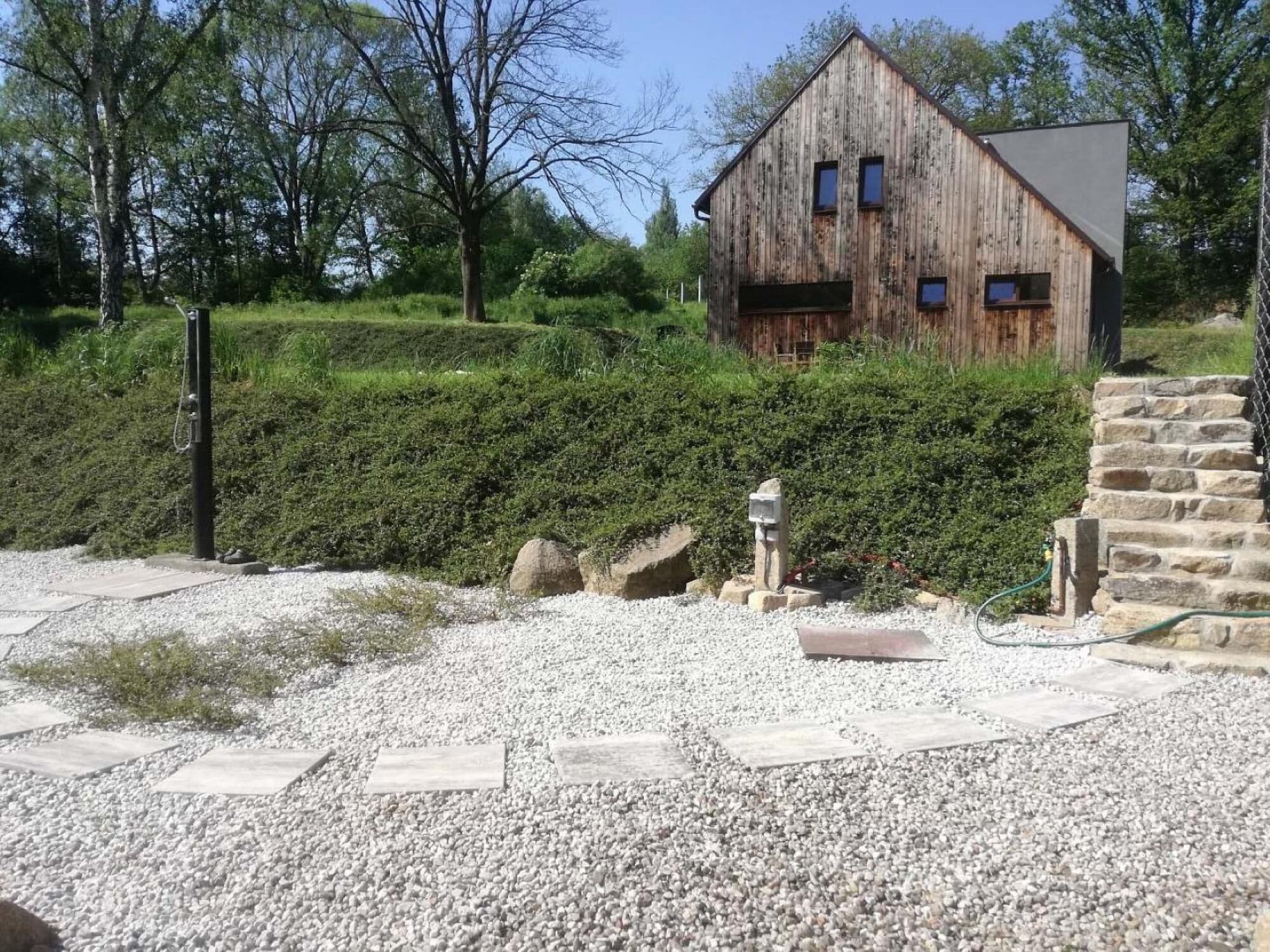 A rustic wooden barn with a sloped roof, surrounded by well-maintained hedges and a gravel path.