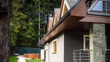 A modern house with a stone foundation, a paved pathway, and a lush green garden.