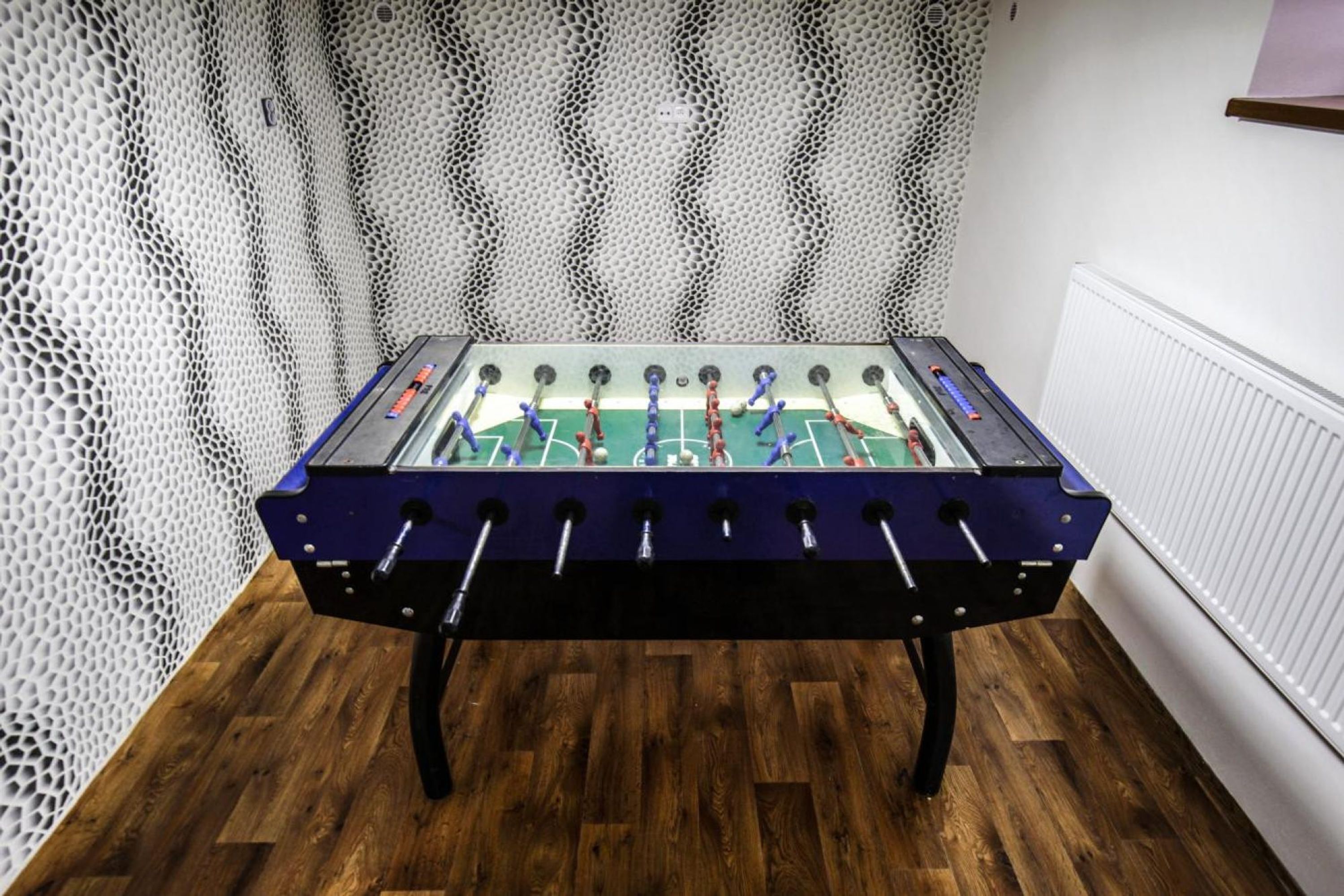 Una mesa de fútbol de mesa en una habitación con suelo de madera y pared blanca con textura.