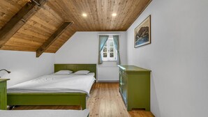 A bedroom with a sloped ceiling, a bed with green headboard, a dresser, and a window with curtains. - Horni Marsov Khk320 in Horn Mar ov (Horni Marsov)