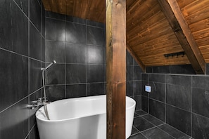 A modern bathroom with a freestanding bathtub, a shower, and a wooden ceiling.