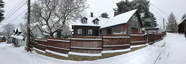 Lumihunnun peittämä puutalo, jonka ympärillä on puinen aita.