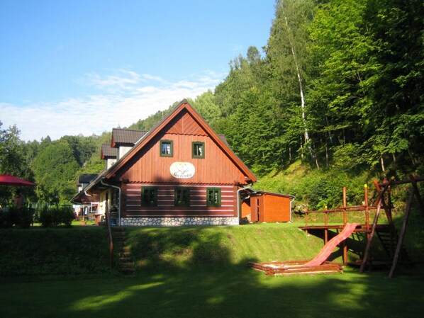 A wooden cabin with a stone foundation, surrounded by lush greenery and a forested hillside. - Rudnik Krp460 in Rudn k (Rudník)