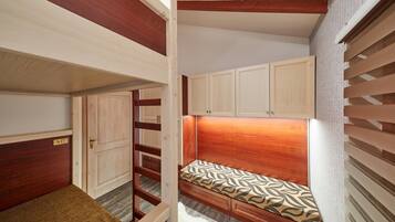 Una habitación pequeña con literas, armarios de madera y un rincón de descanso.