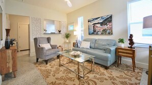 A living room with a ceiling fan, a sofa, a coffee table, and a painting on the wall. - Lakeside - Lake Davis Art Deco Cottage 5C (Orlando)