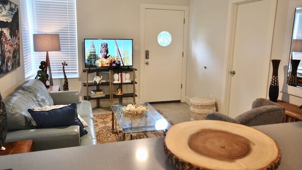 A living room with a sofa, a coffee table, a TV, and a door with a circular window. - Lakeside - Lake Davis Art Deco Cottage 5C (Orlando)
