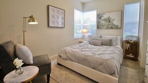 A bedroom with a bed, a chair, a lamp, a picture frame, and a window with blinds. - Lakeside - Lake Davis Art Deco Cottage 5C (Orlando)
