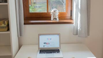 A room with a white desk, a laptop, a window with a view of trees, and a shelf with books.
