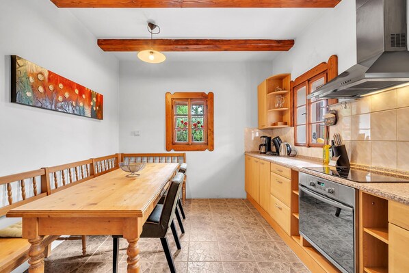 Una cocina con armarios de madera, horno empotrado y comedor con mesa y sillas de madera.