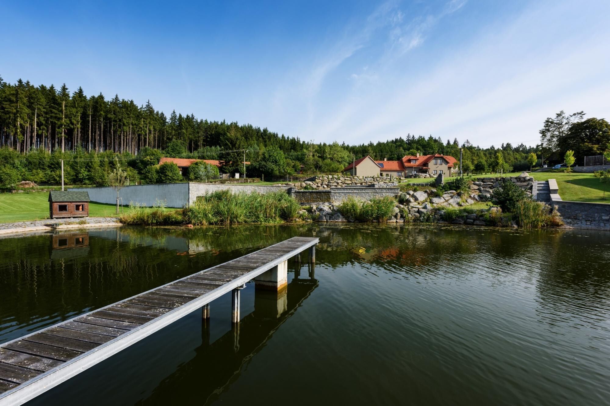 Une propriété au bord du lac, dotée d’un quai, d’un petit chalet et d’une maison principale avec un toit rouge.