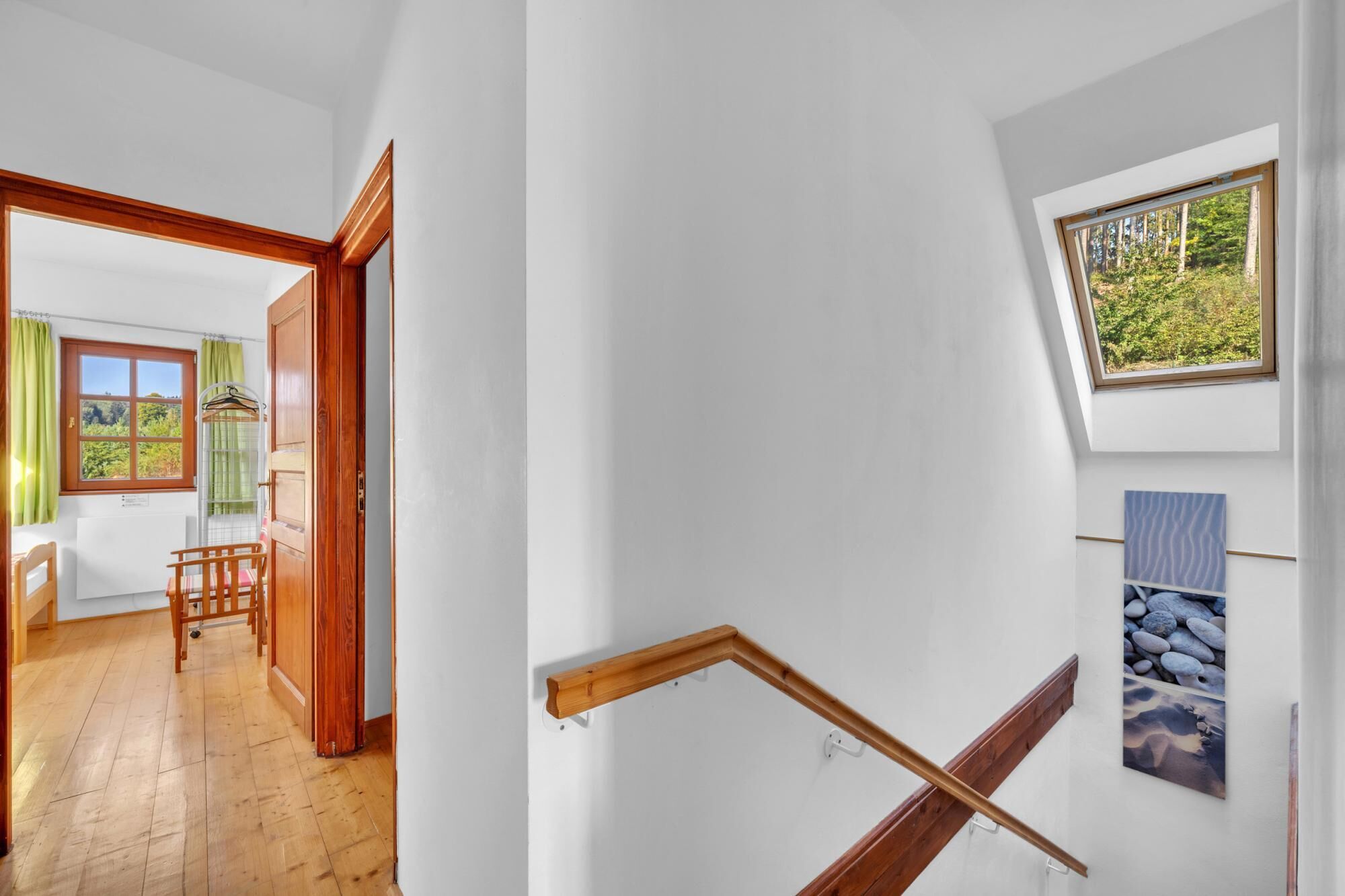 Un escalier avec des rampes en bois, une petite fenêtre donnant sur la verdure et un tableau accroché au mur.