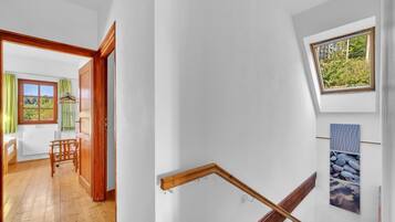 Un escalier avec des rampes en bois, une petite fenêtre donnant sur la verdure et un tableau accroché au mur.