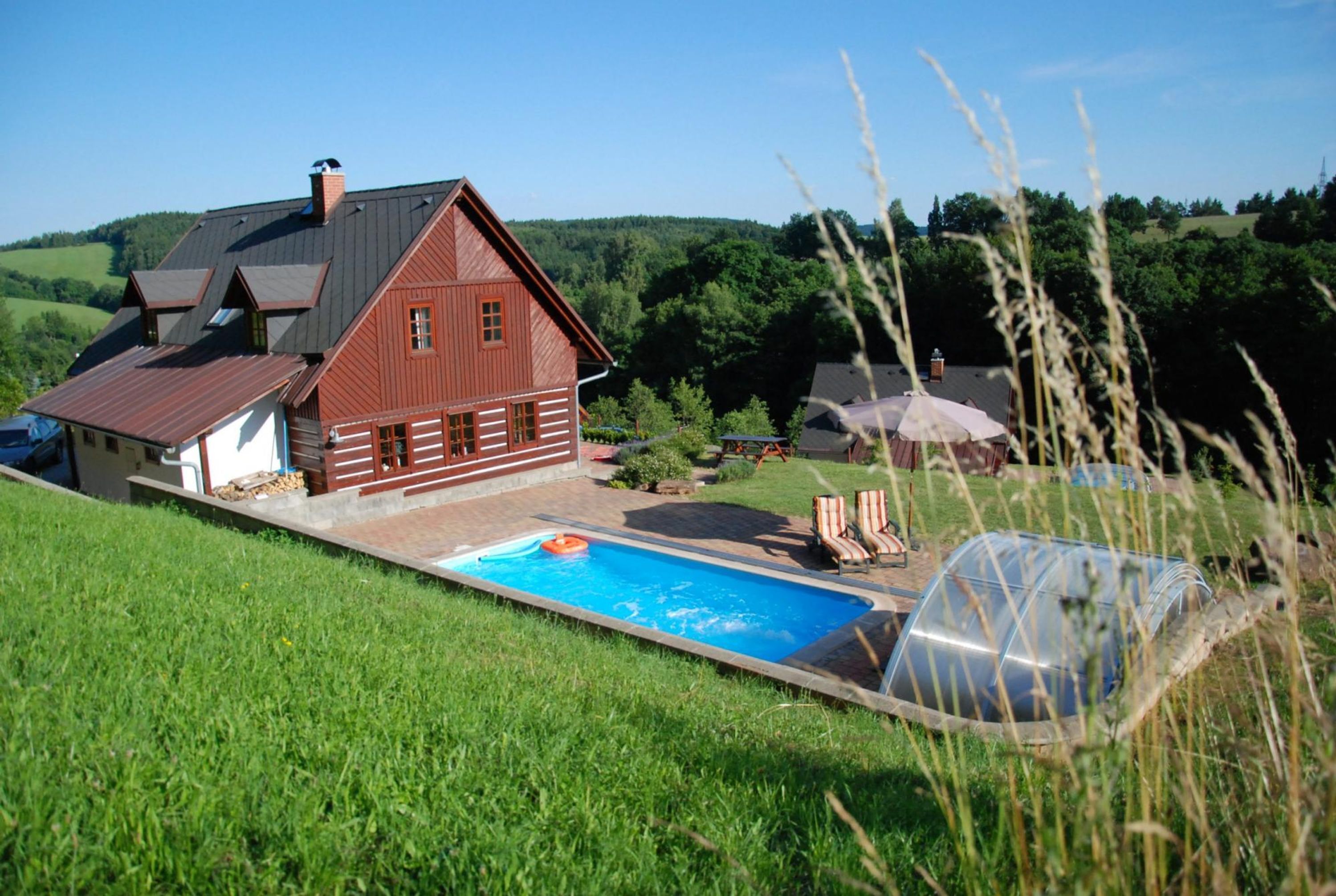 A house with a swimming pool, surrounded by a lush green landscape.