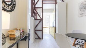 A modern interior with a staircase, a dining area with a table and chairs, and a bookshelf with books.