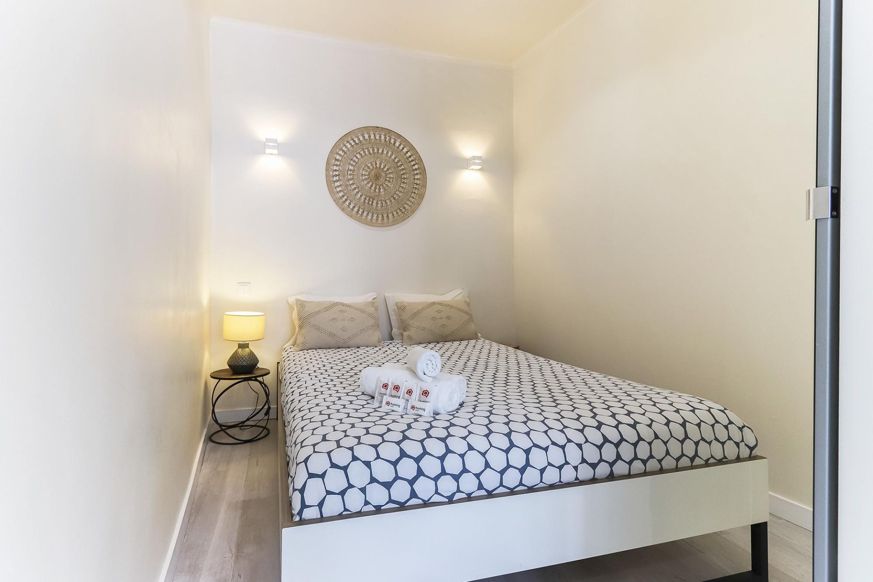A neatly made bed with a patterned bedspread, two pillows, and a decorative wall piece above it.