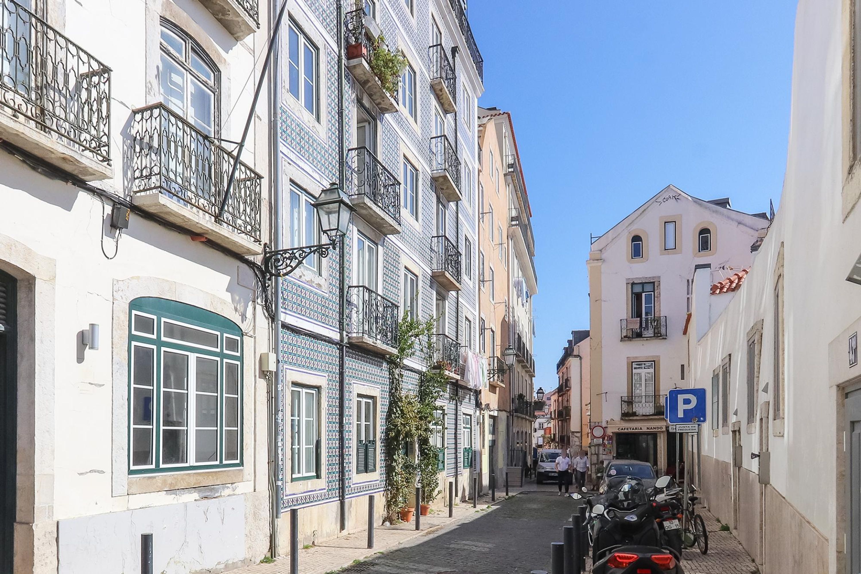 A narrow street lined with multi-story buildings, some with balconies and potted plants.