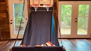 Un panier de basket avec un filet, deux portes dotées de panneaux en verre et une vue sur une terrasse en bois.
