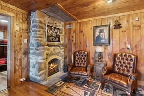 A cozy room with a stone fireplace, leather armchairs, and a clock repair sign. - Whiskey Ridge Lodge ~ Rustic Luxe Cabin with Hot Tub, Game Lounge & Epic Mountain Views (Gatlinburg)