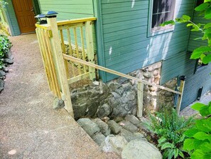 Eine Holztreppe führt zu einem Steinfundament eines Hauses mit grüner Fassade.