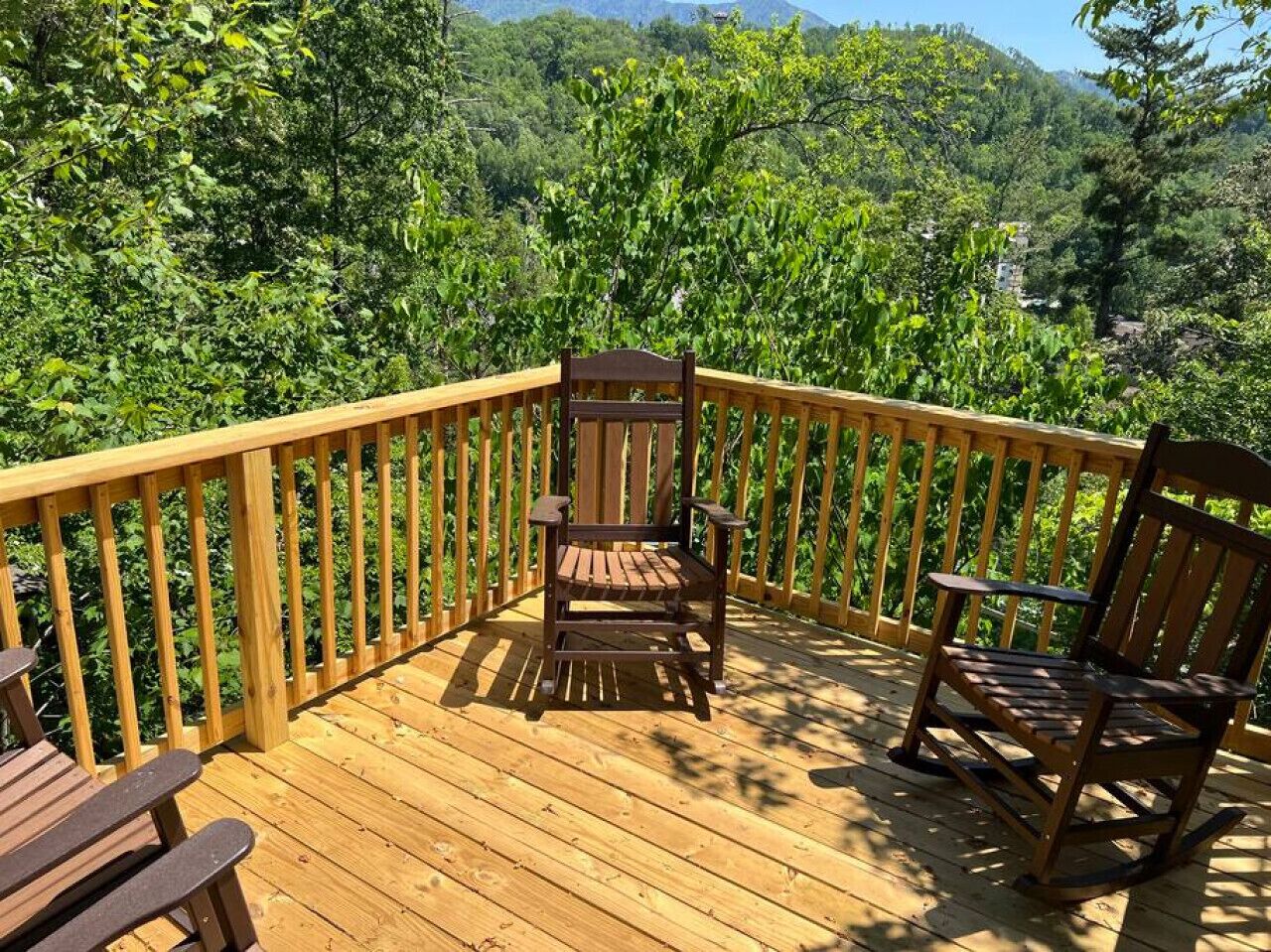 Eine Holzterrasse mit zwei Holzstühlen und einem Tisch, umgeben von einem Geländer, mit Blick auf ein bewaldetes Gebiet.