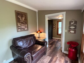 Ein Wohnzimmer mit einer Ledersofa, einer Lampe und einem Flur, der in einen anderen Raum führt.