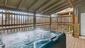 Un bain à remous sur une terrasse en bois, avec une clôture en bois et un bâtiment en arrière-plan.