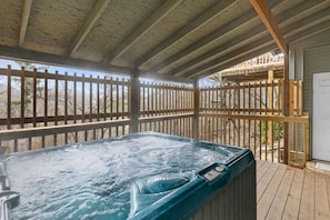 A hot tub on a wooden deck with a wooden fence and a building in the background.