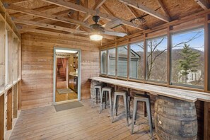 A wooden interior with a bar area, stools, and a view through large windows. - Whiskey Ridge Lodge ~ Rustic Luxe Cabin with Hot Tub, Game Lounge & Epic Mountain Views (Gatlinburg)