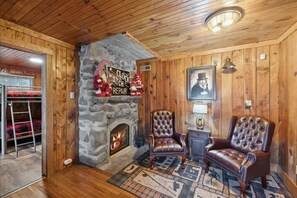 A cozy room with a stone fireplace, two leather armchairs, a wooden ceiling, and a framed picture on the wall.