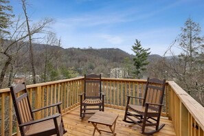A wooden deck with three rocking chairs and a small table, overlooking a mountainous landscape.