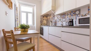 A modern kitchen with white cabinets, a wooden dining table, and a potted plant. - Bairro Alto Stylish by Homing (Lisbon)