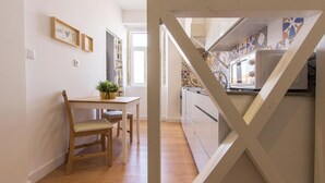 A modern kitchen with a wooden table and chairs, a potted plant, and a view of the adjacent dining area. - Bairro Alto Stylish by Homing (Lisbon)