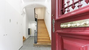 Uma escadaria leva a um patamar com uma porta vermelha e um corrimão preto.