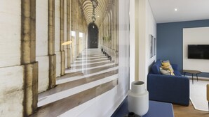 Uma sala de estar moderna com um sofá azul, um vaso branco grande e uma televisão de tela plana na parede.
