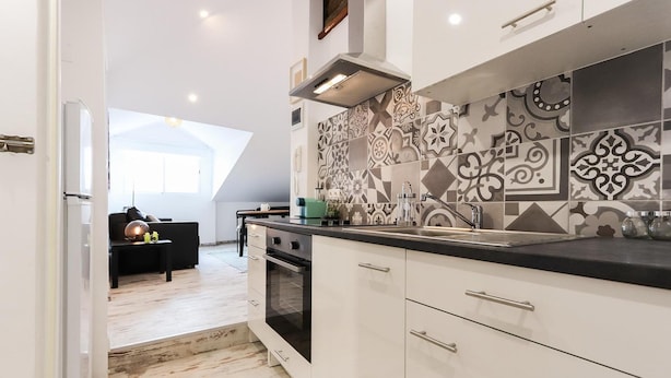 Een moderne keuken met witte kastjes, een zwart aanrecht en betegelde spatwand met patroon.