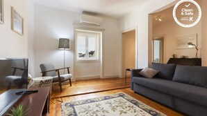 A living room with a sofa, a chair, a TV, a lamp, and a window. - Chiado Views by Homing (Lisbon)