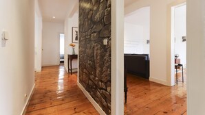 A hallway with wooden flooring, a stone accent wall, and a dark-colored sofa in the background. - Chiado Views by Homing (Lisbon)