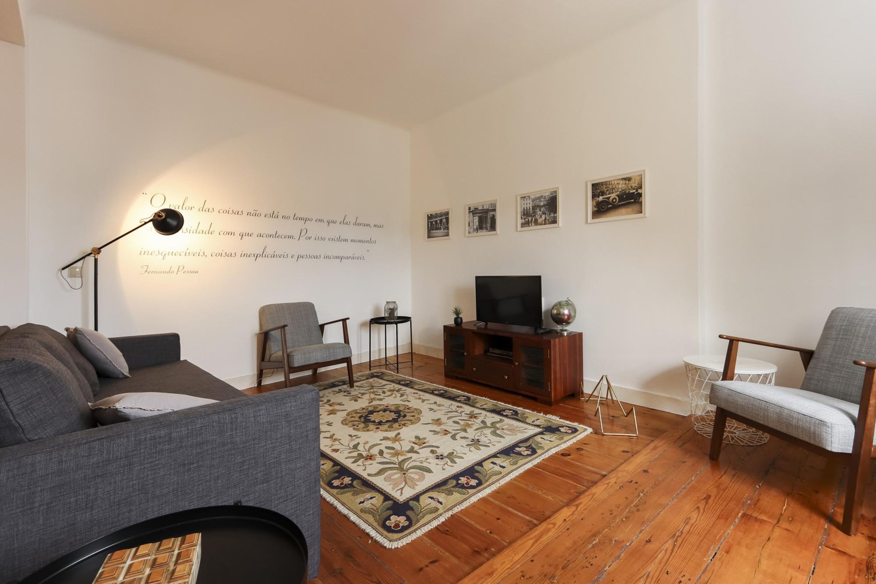 Una sala de estar con sofá, sillones, televisor, alfombra y decoración en las paredes.